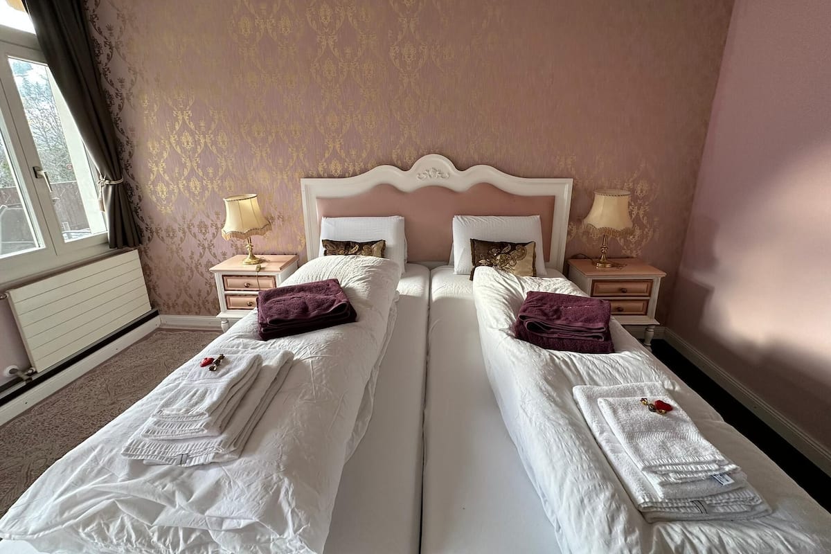 A double bed room with a white headboard, two bedside tables with lamps, and a window with curtains.