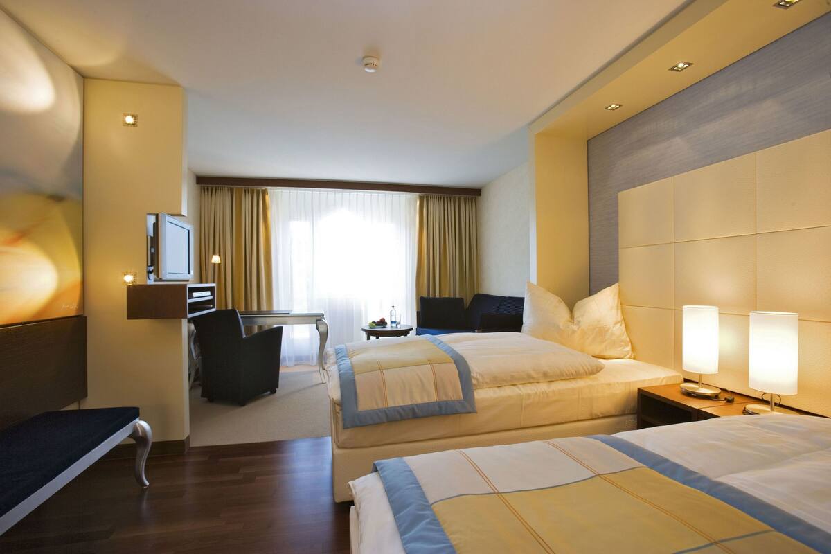 A hotel room with two beds, a desk, a chair, and a TV.