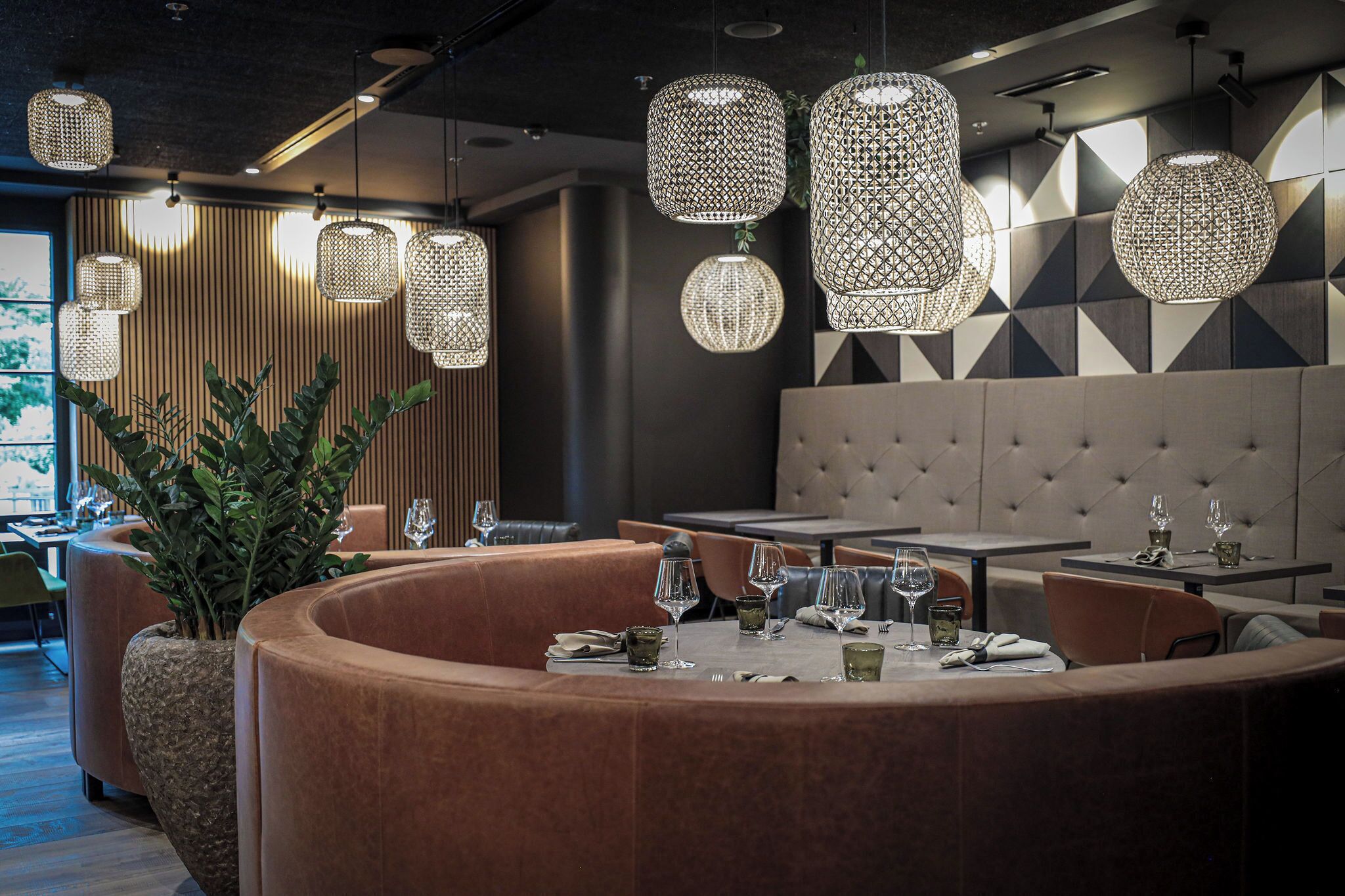 Un restaurante moderno con mesas redondas, asientos acolchados e iluminación decorativa colgante.