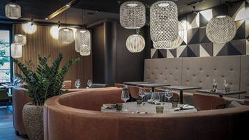 Un restaurante moderno con mesas redondas, asientos acolchados e iluminación decorativa colgante.