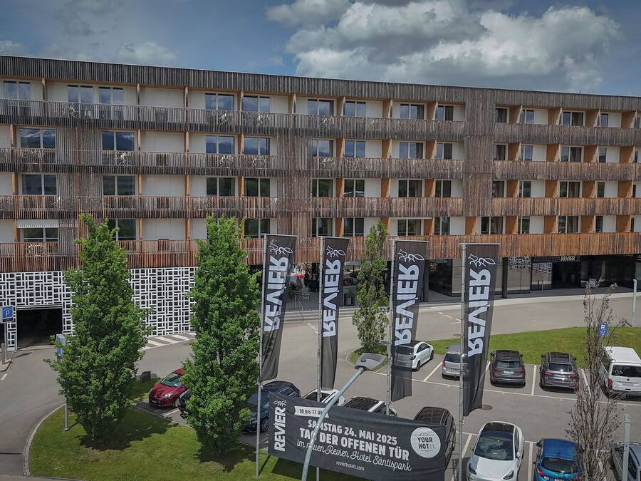 A modern hotel with multiple balconies, a parking area, and several flags indicating amenities.