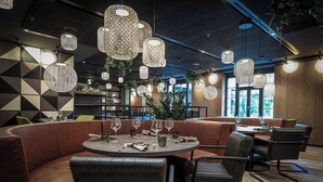 Interior moderno de restaurante con mesas redondas, asientos de cuero e iluminación decorativa colgante.