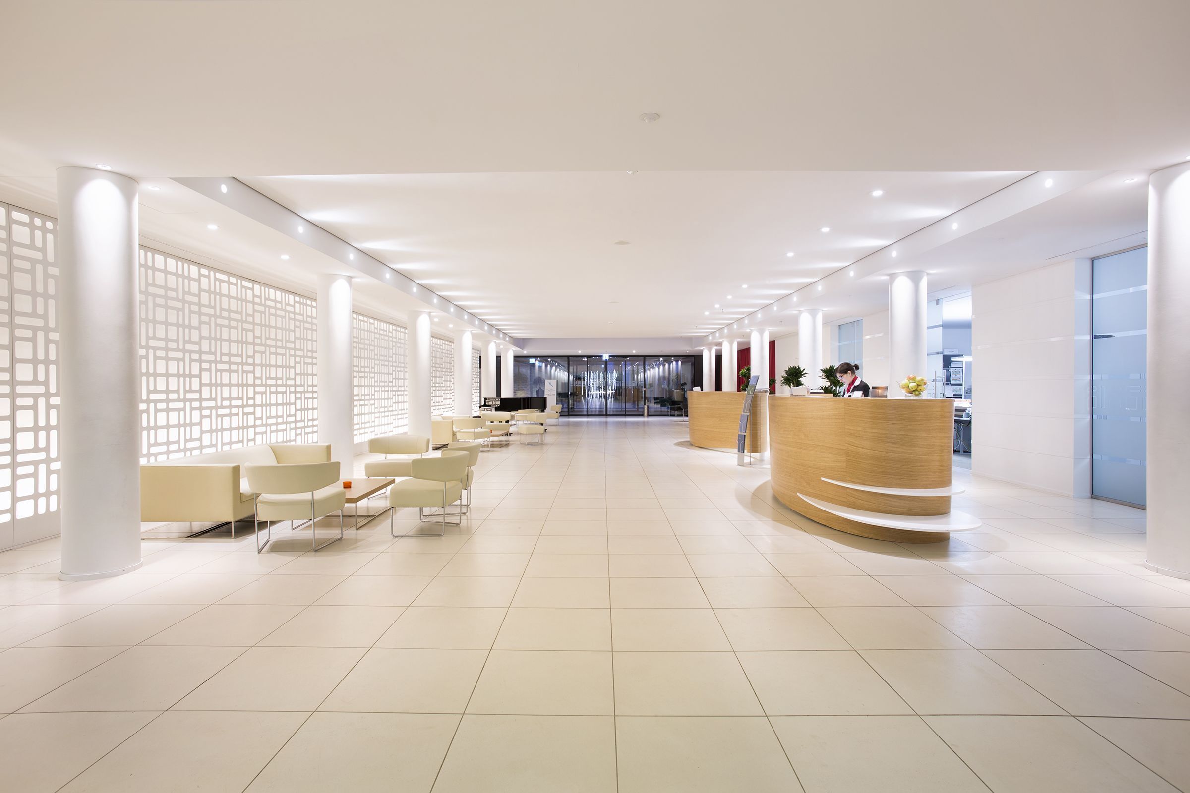 Eine geräumige Lobby mit Empfangstresen, einer Sitzecke und einem modernen Design, erkennbar an den weißen Wänden und Säulen.