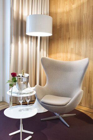 A modern room with a light grey upholstered armchair, a white side table with a champagne bottle and glasses, and a large floor lamp.