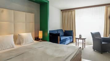 Quarto de hotel com uma cama grande, um sofá, uma poltrona, uma mesa pequena e um abajur.