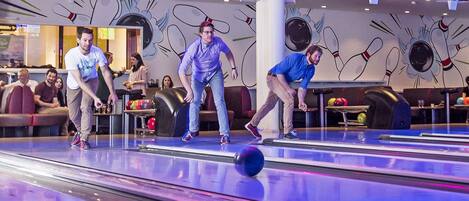 A bowling alley with multiple lanes and a colorful mural on the wall.