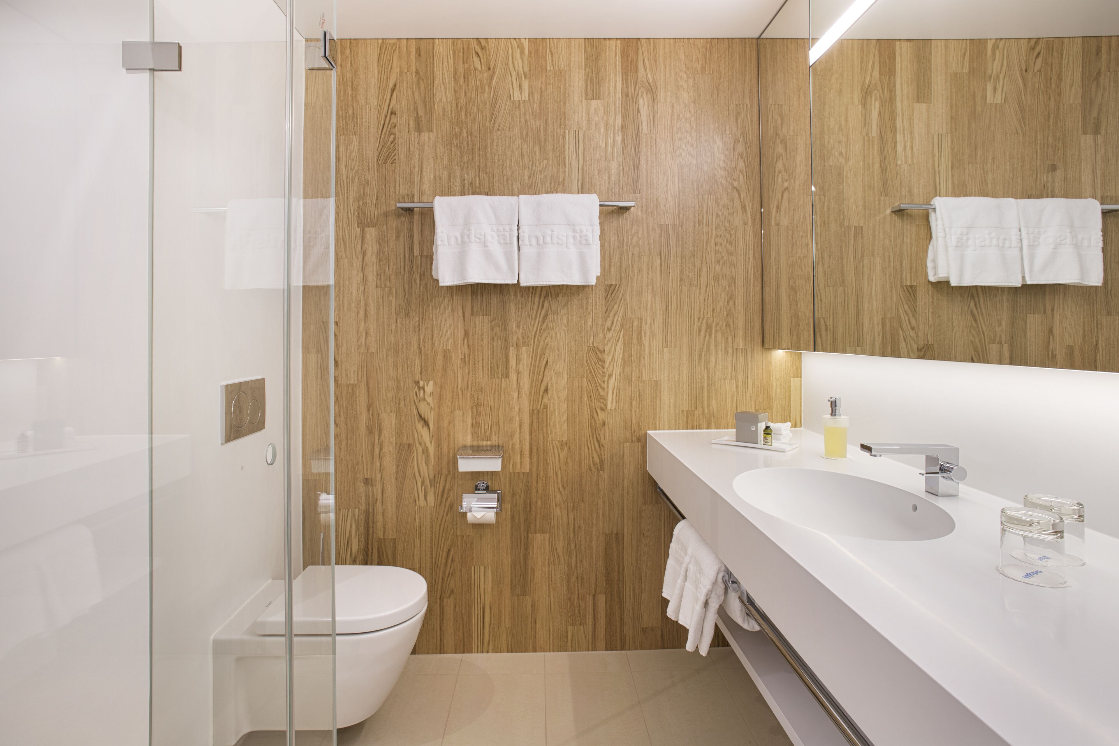 Un baño moderno con pared de madera, cabina de ducha con vidrio, lavabo blanco y un inodoro.