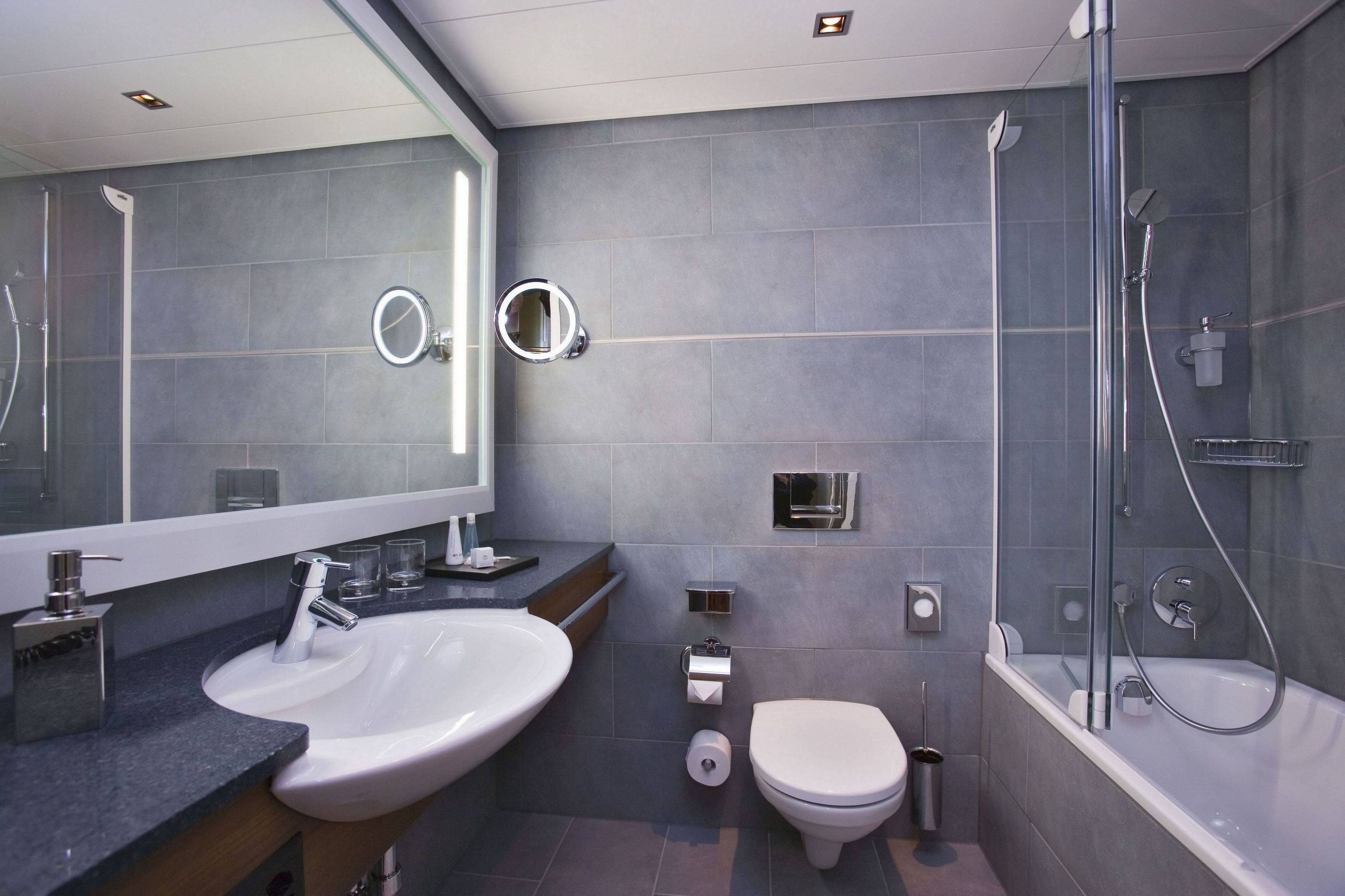 A modern bathroom with a large mirror, a sink, a toilet, and a shower area.