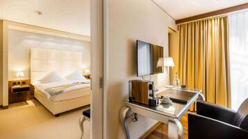 A hotel room with a bed, bedside table with a lamp, a desk with a laptop, and a chair.