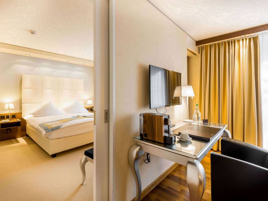 A hotel room with a bed, bedside table with a lamp, a desk with a laptop, and a chair.