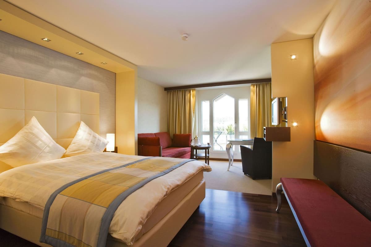 A hotel room with a large bed, a desk, a chair, and a view of the outdoors.