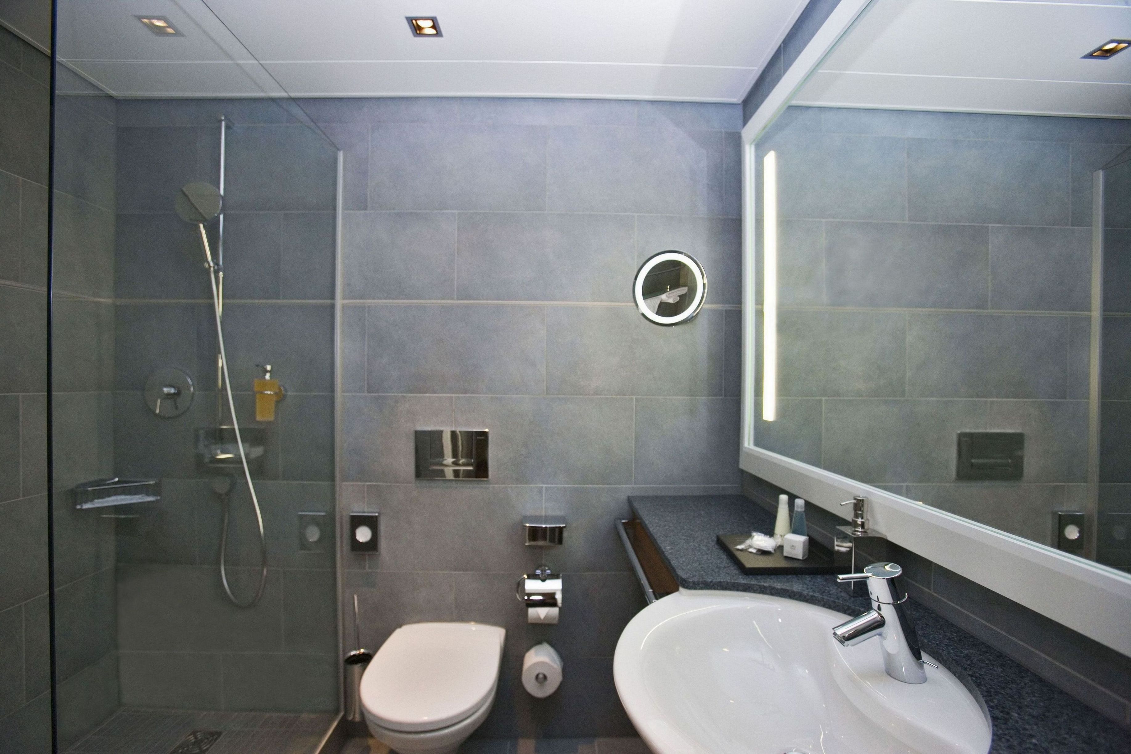 A modern bathroom with a glass-enclosed shower, a toilet, a sink, and a large mirror.