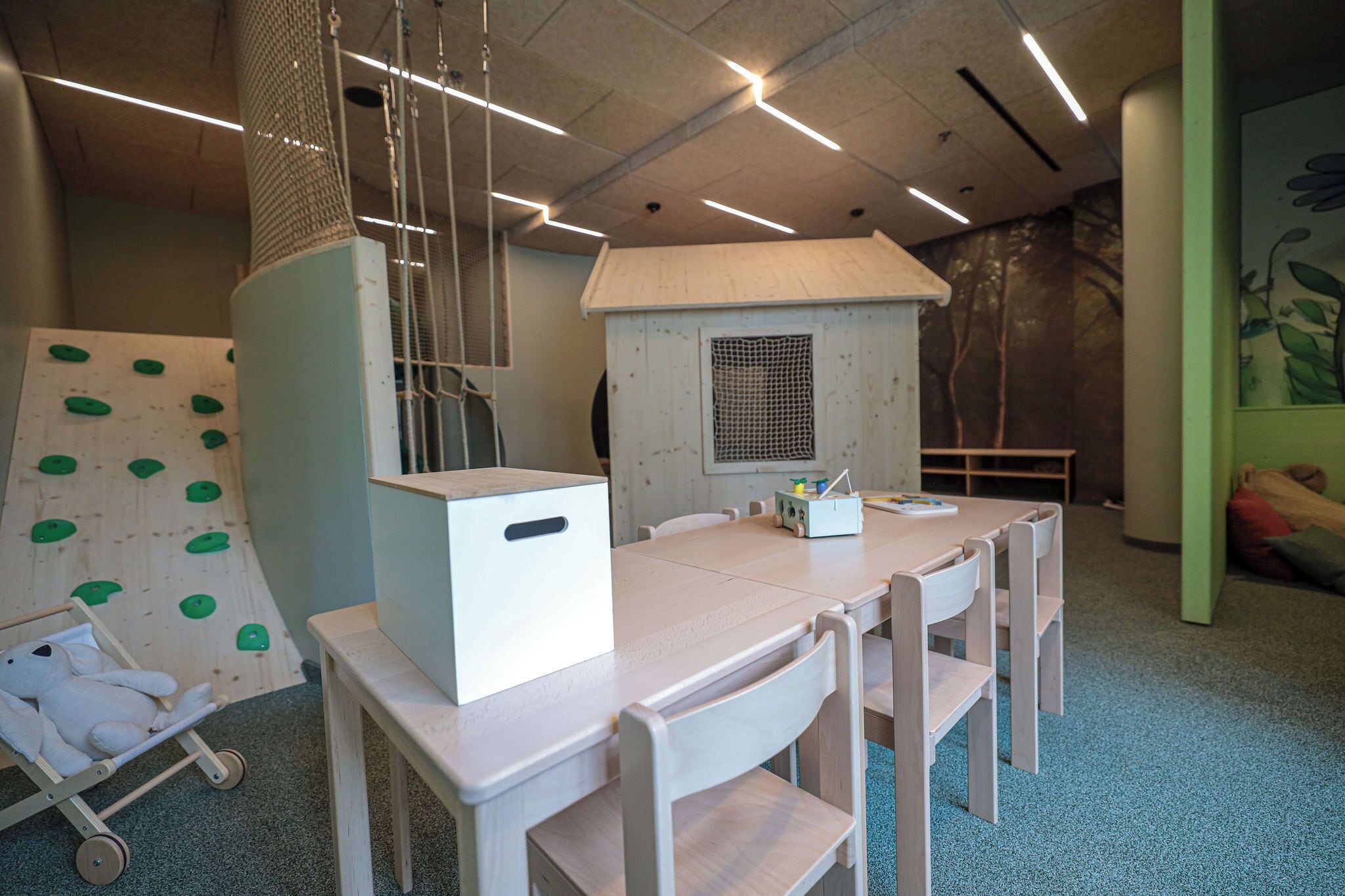 Een speelruimte met klimmuren, een poppenhuis en een tafel met stoelen.