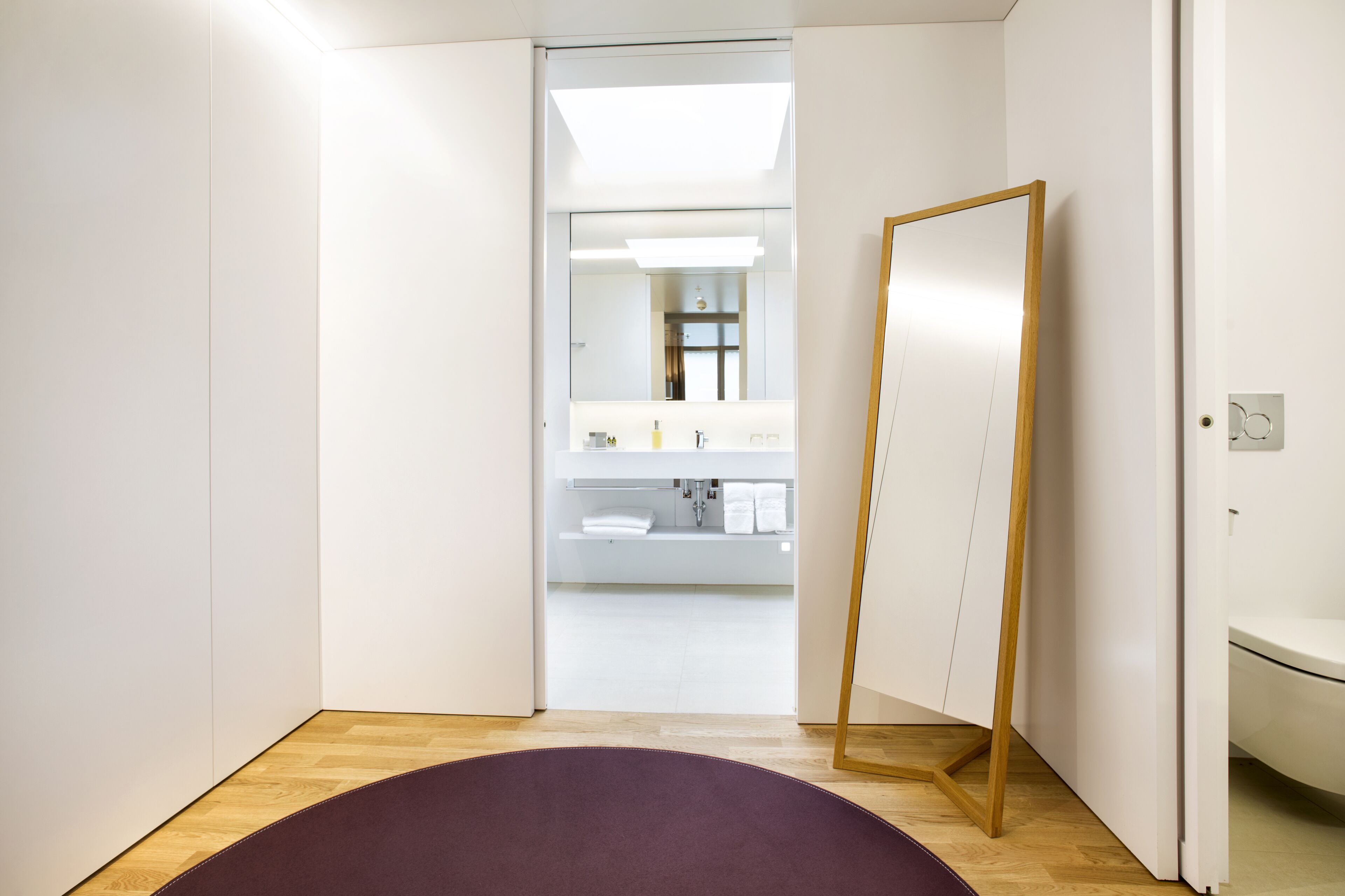 Une salle de bain moderne avec un grand miroir, des meubles blancs et un plancher en bois.