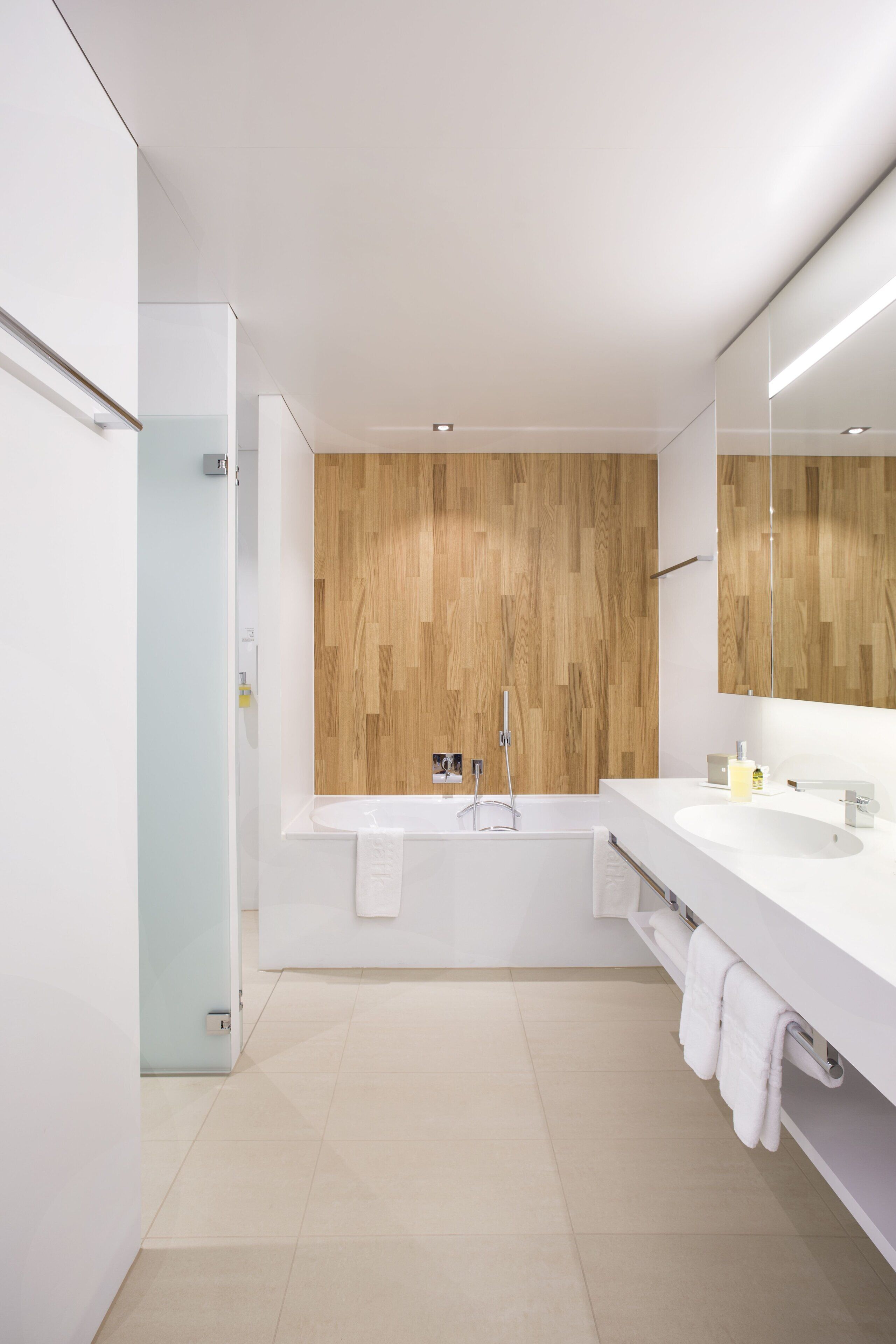 A modern bathroom with a wooden wall panel, a bathtub, a sink, and a large mirror.