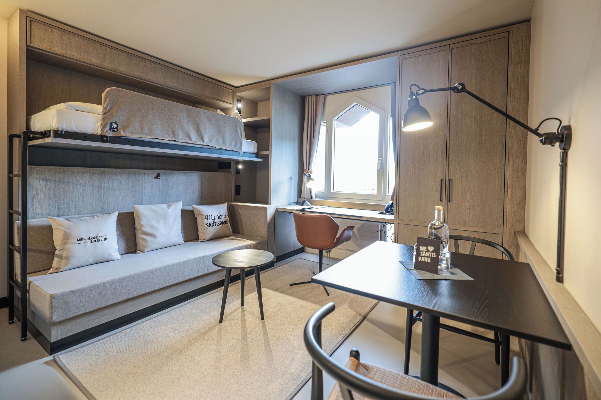 A compact room with bunk beds, a sofa, a dining table, and a small window.