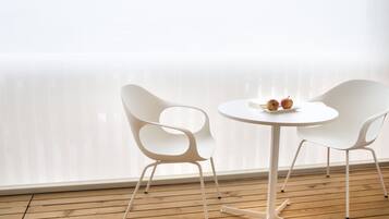 A room with a wooden floor, white chairs, a small round table, and a window with blinds.