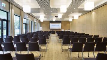 Ein Konferenzraum mit Tischen und Stühlen, einer Projektionsleinwand und einer Holzwand.