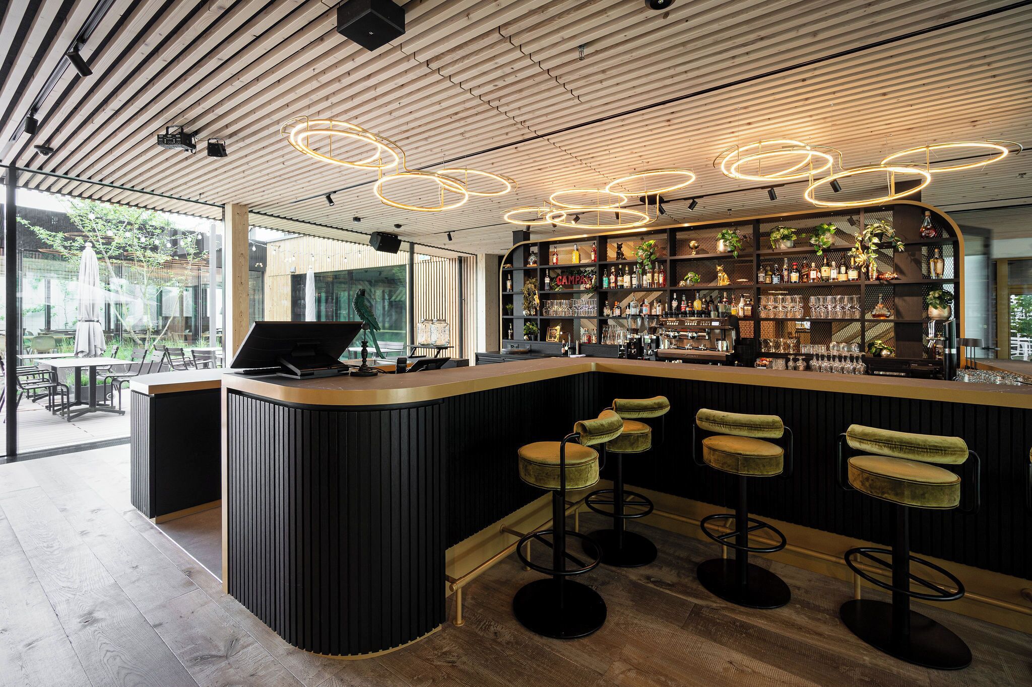 A modern bar area with a curved counter, bar stools, and a well-stocked shelf with various bottles and glasses.