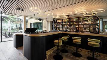 A modern bar area with a curved counter, bar stools, and a well-stocked shelf with various bottles and glasses.