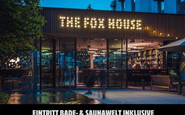 A modern bar with a glass facade and a pool area in the foreground.