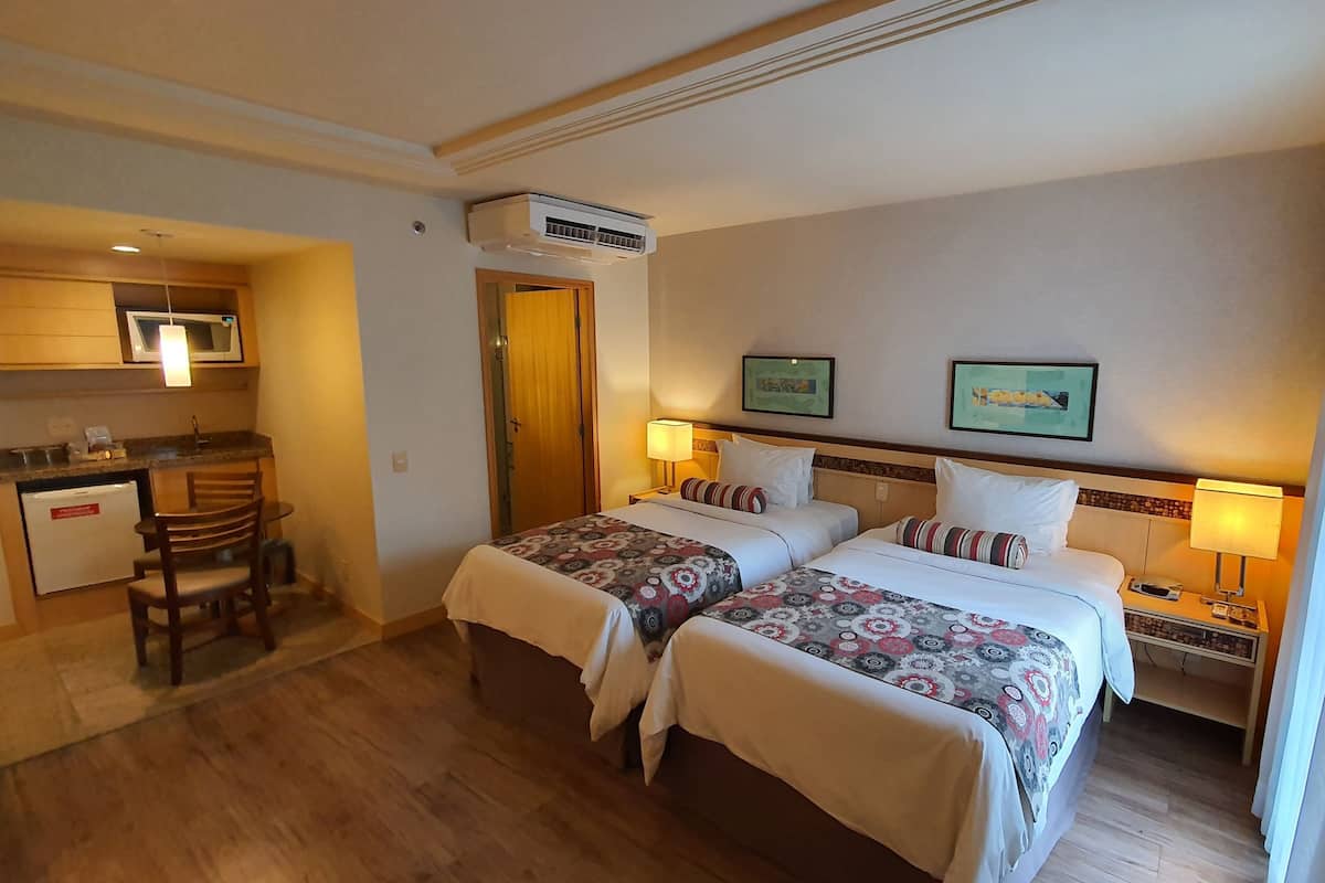 Quarto de hotel com duas camas, uma kitchenette e um banheiro.