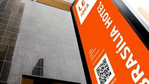 Un edificio alto de diseño moderno, con un llamativo letrero naranja con texto blanco que anuncia un hotel.