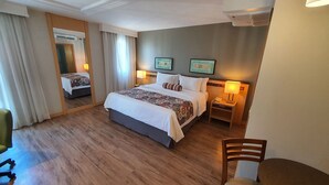 Una habitación de hotel con una cama grande, una mesita de noche con lámpara, una silla y un espejo.