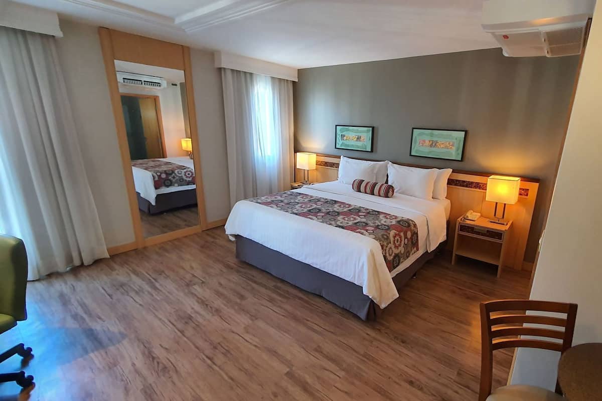Quarto de hotel com uma cama grande, mesas de cabeceira, um espelho e obras de arte nas paredes.