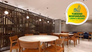 Un moderno vestíbulo de hotel con mesas redondas y sillas de madera, un separador decorativo de madera y el logotipo de 'Responsible Tourism'.