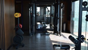 Un gimnasio con equipo de ejercicio, piso de madera y ventanas amplias que dejan entrar luz natural.