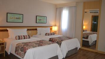 A hotel room with two beds, a nightstand, a mirror, and two framed pictures on the wall.