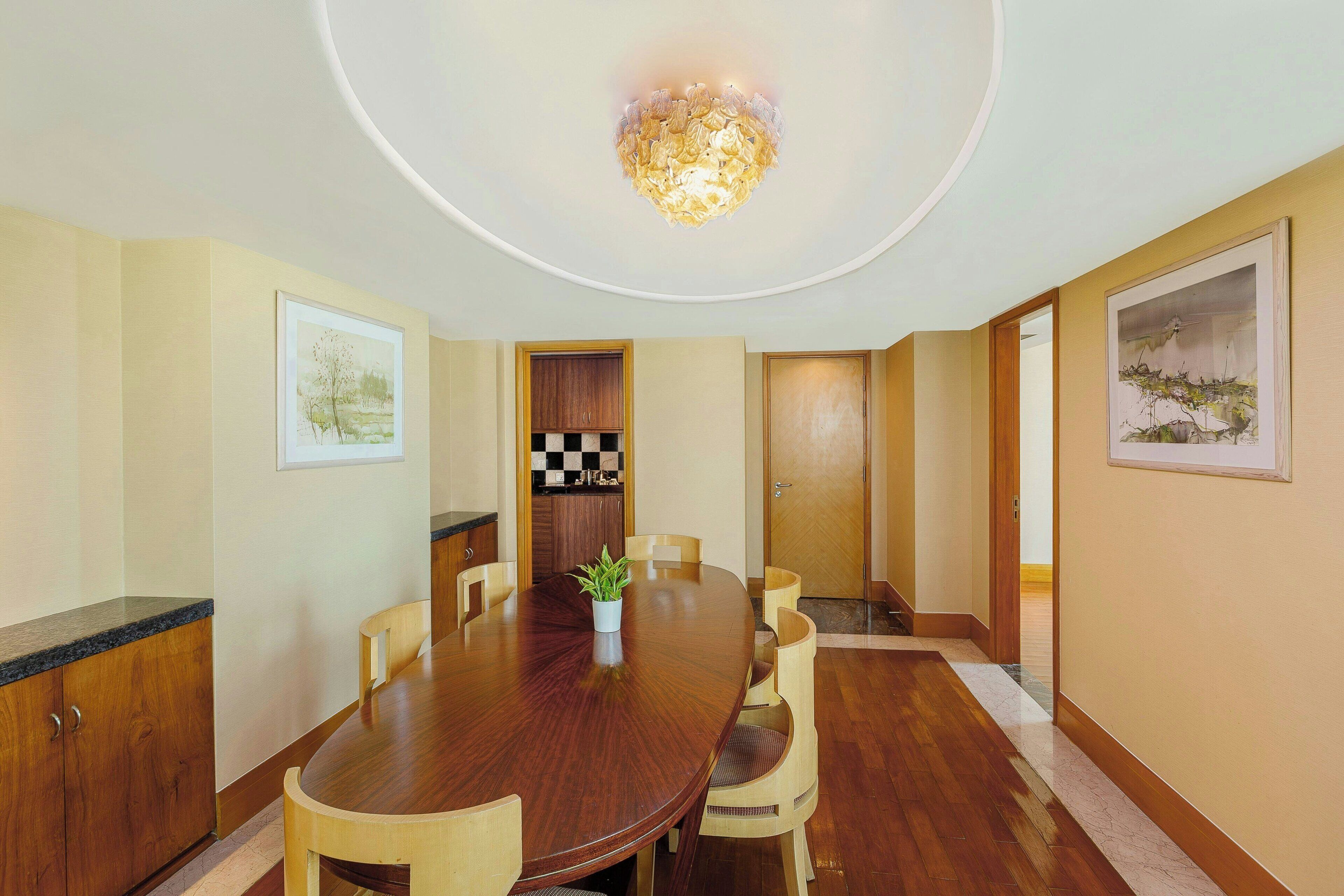 A conference room with a wooden table, chairs, a potted plant, and framed artwork on the walls.