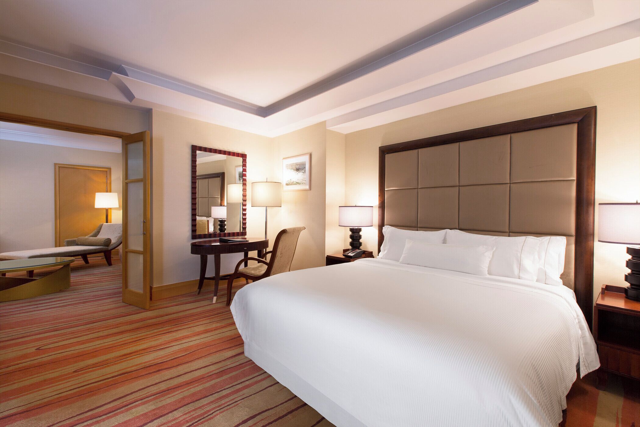 Una habitación de hotel con una cama grande, un escritorio con una silla, una mesita y un espejo.