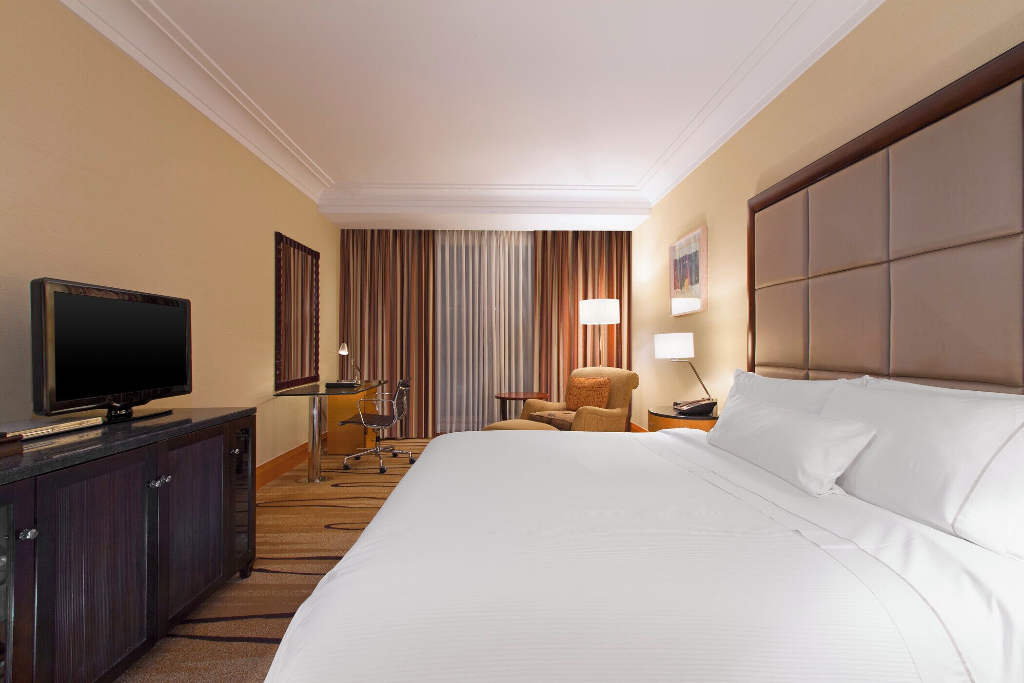 Une chambre d’hôtel avec un grand lit, un téléviseur posé sur un meuble, une chaise, un bureau et une lampe.