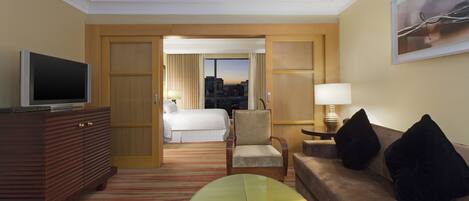 A hotel room with a bed, a TV, a sofa, a chair, and a table.