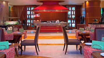 Un vestíbulo de hotel con una zona de bar central, varias mesas de comedor con sillas y una gran lámpara de araña moderna.