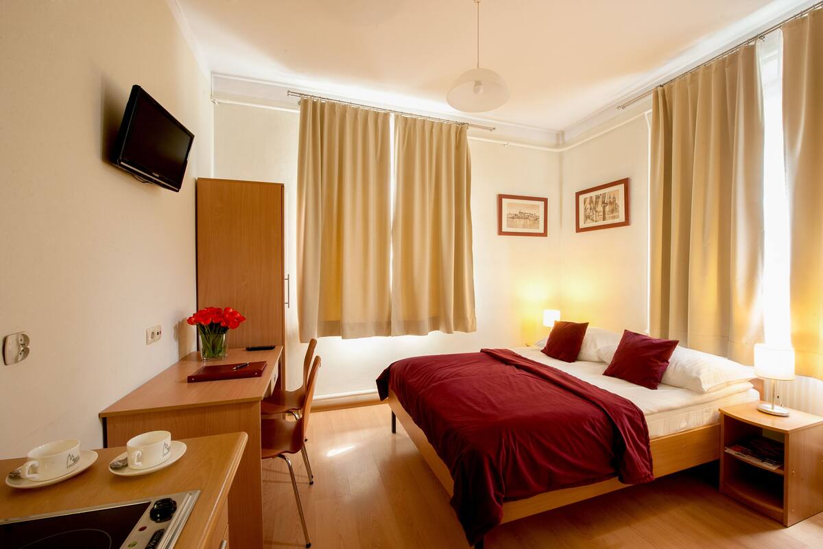 A hotel room with a bed, bedside table, desk, chair, and a television on the wall.