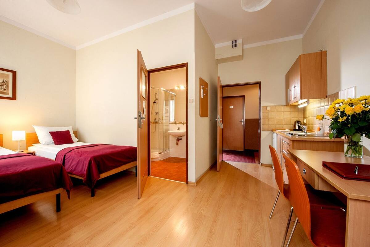 A hotel room with two beds, a shower, a sink, and a small kitchen area.