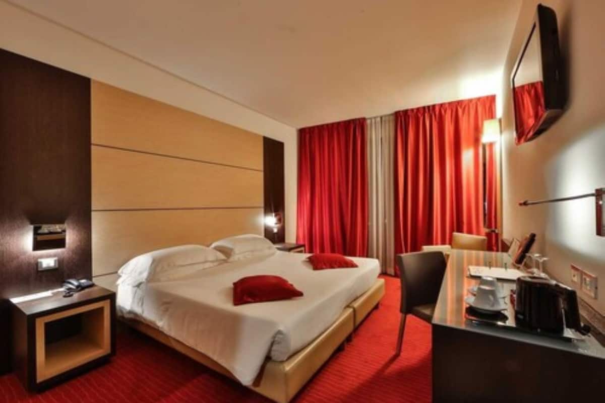 Une chambre d’hôtel avec un lit, un bureau, une chaise et un rideau rouge.