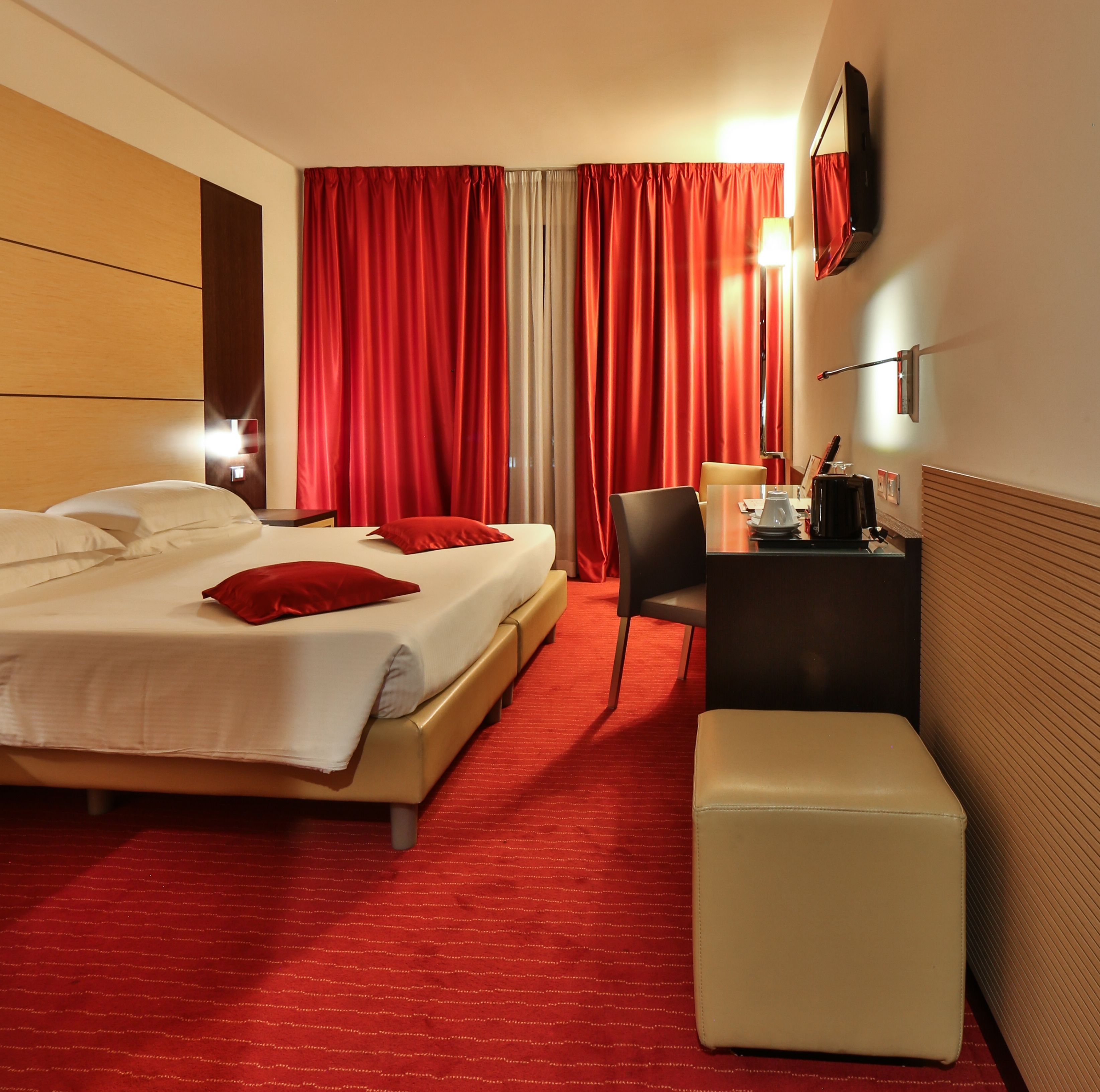 A hotel room with a bed, a desk, a chair, a lamp, and a TV on the wall.
