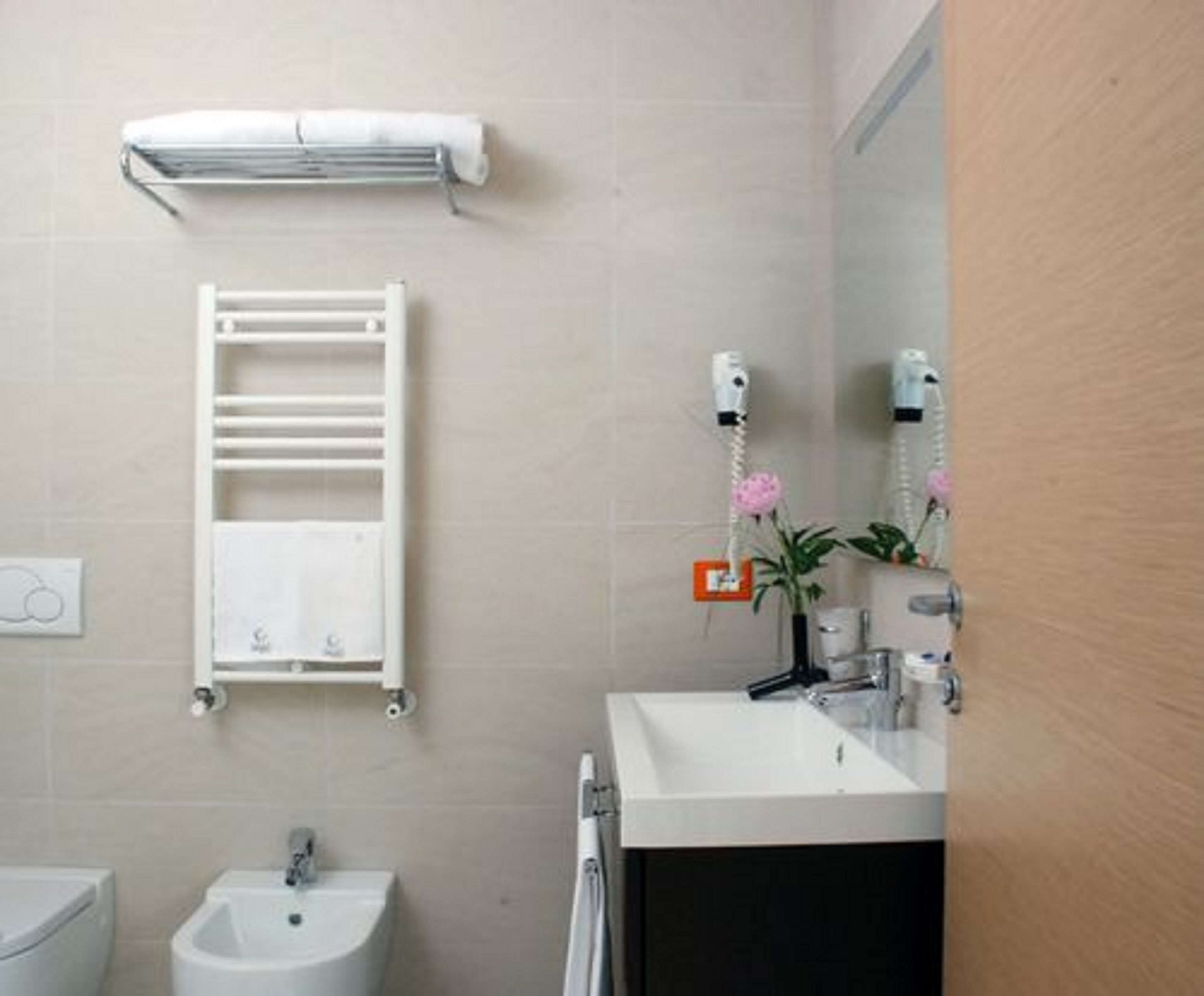 Un baño con lavamanos blanco, bidé, toallero y espejo con una toalla colgada.