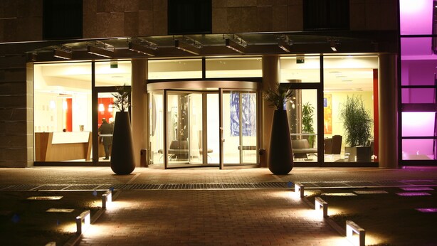 A hotel entrance with a glass door, a brick pathway, and potted plants.