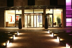 L’entrée d’un hôtel avec une porte en verre, un chemin en briques et des plantes en pot.