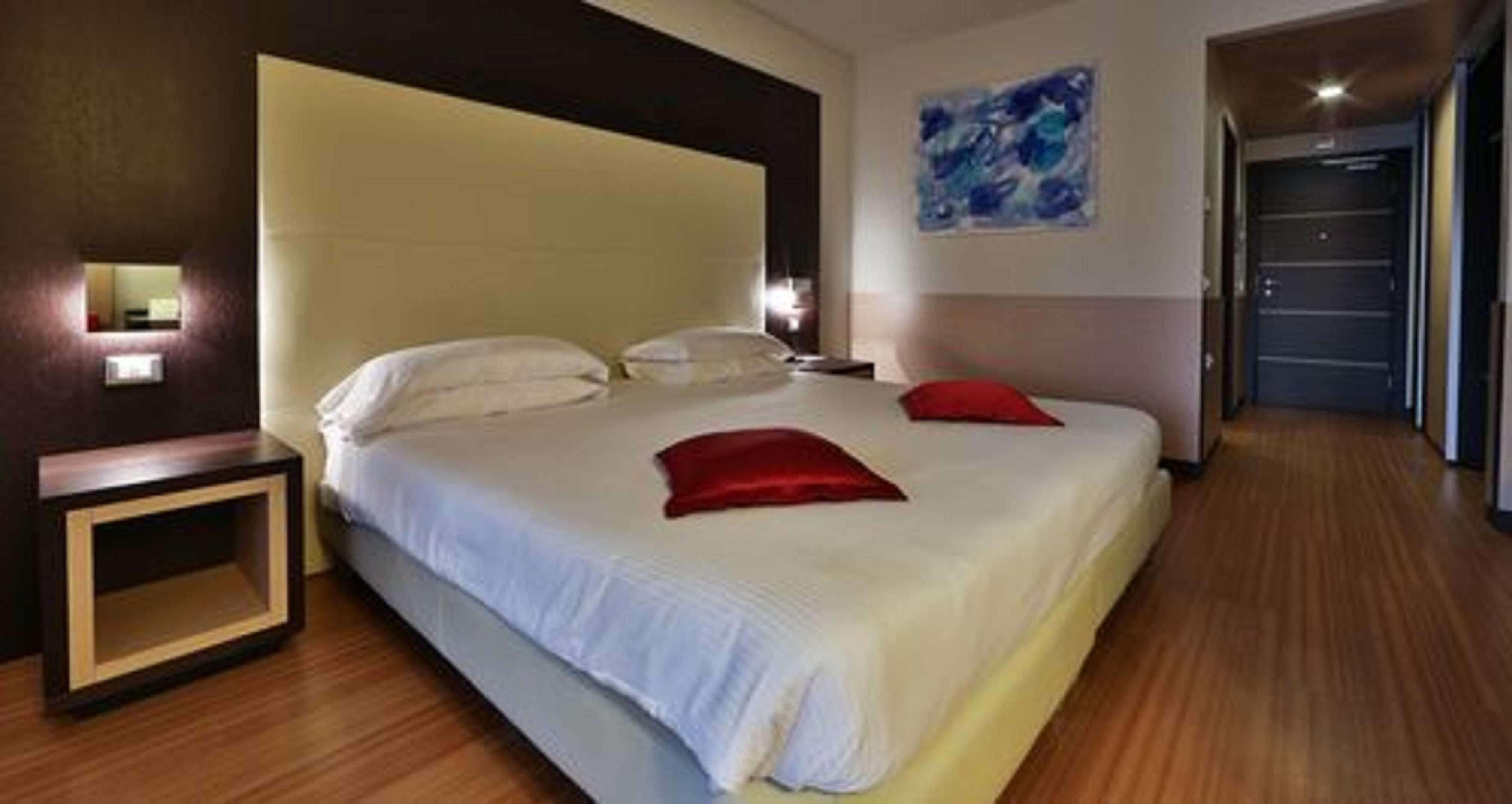 A hotel room with a large bed, bedside tables, a painting on the wall, and a wooden floor.