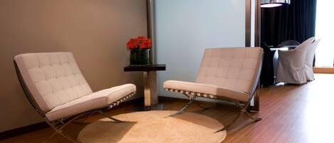 Una habitación moderna con dos sillones de cuero blanco, una mesita con un jarrón de flores rojas y una alfombra redonda sobre un suelo de madera.
