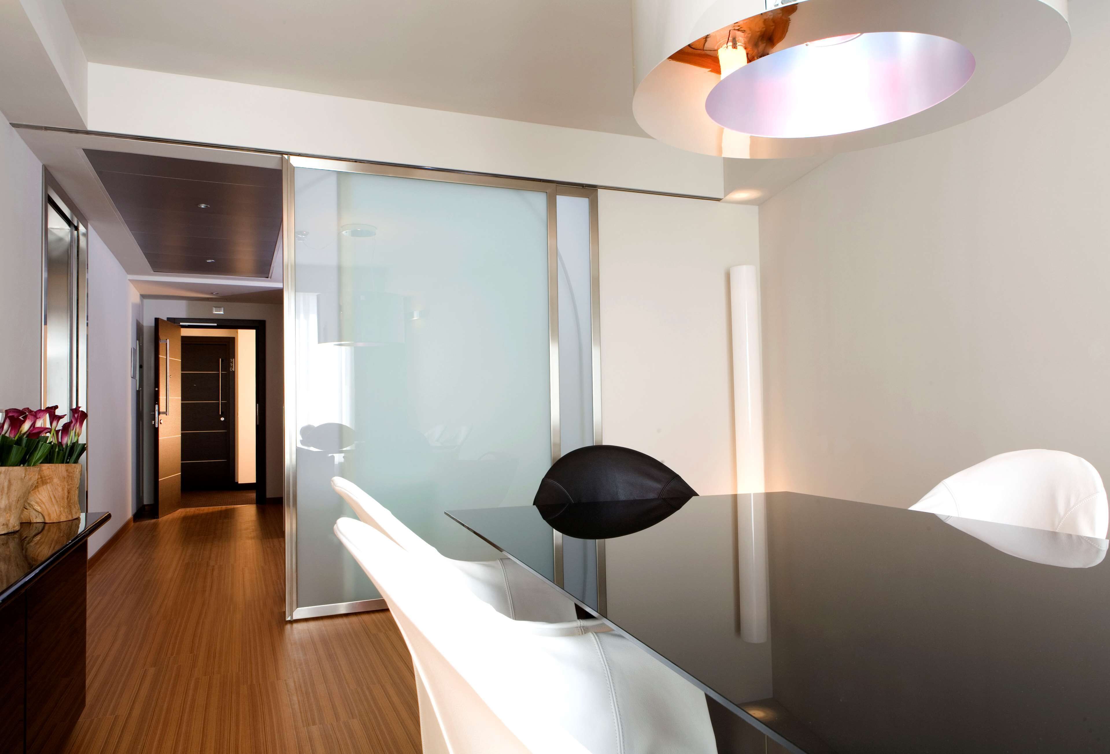 Una habitación de hotel moderna con un separador de vidrio, suelo de madera, sofá blanco y lámpara negra.