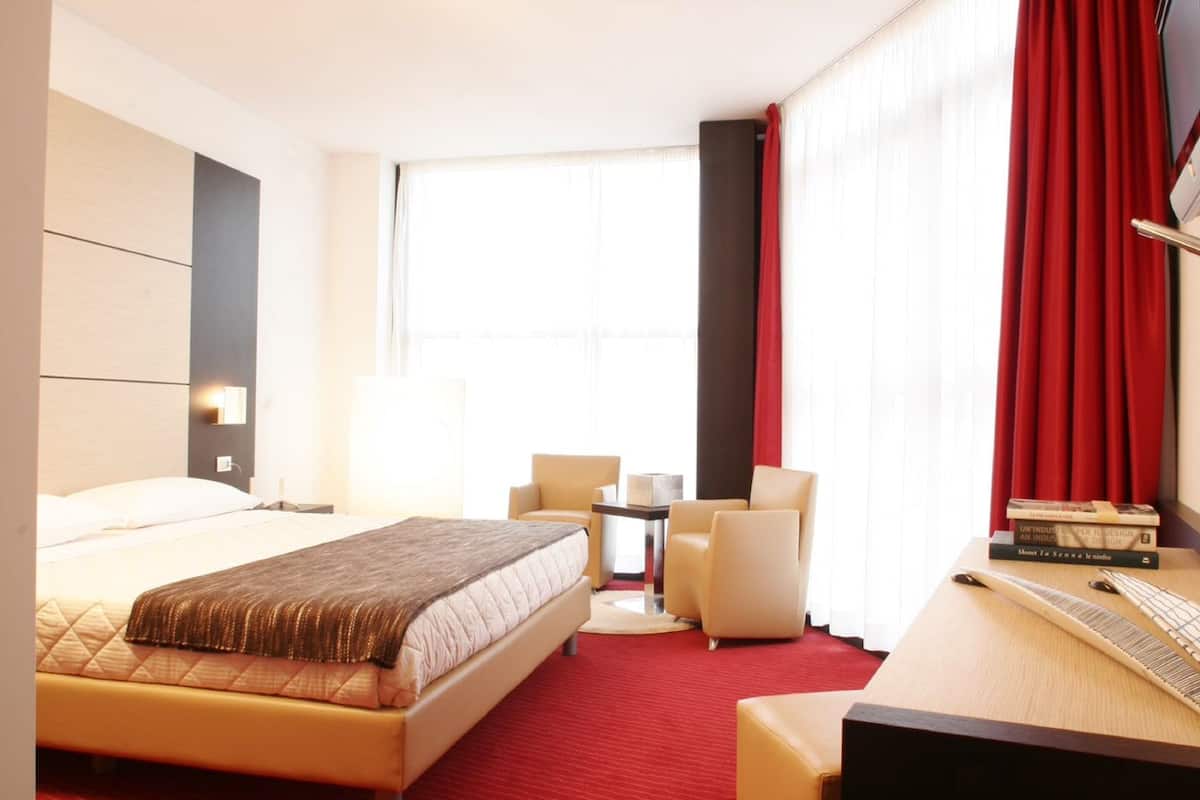 Une chambre d’hôtel comprenant un lit, deux fauteuils, une petite table et un bureau avec un clavier.