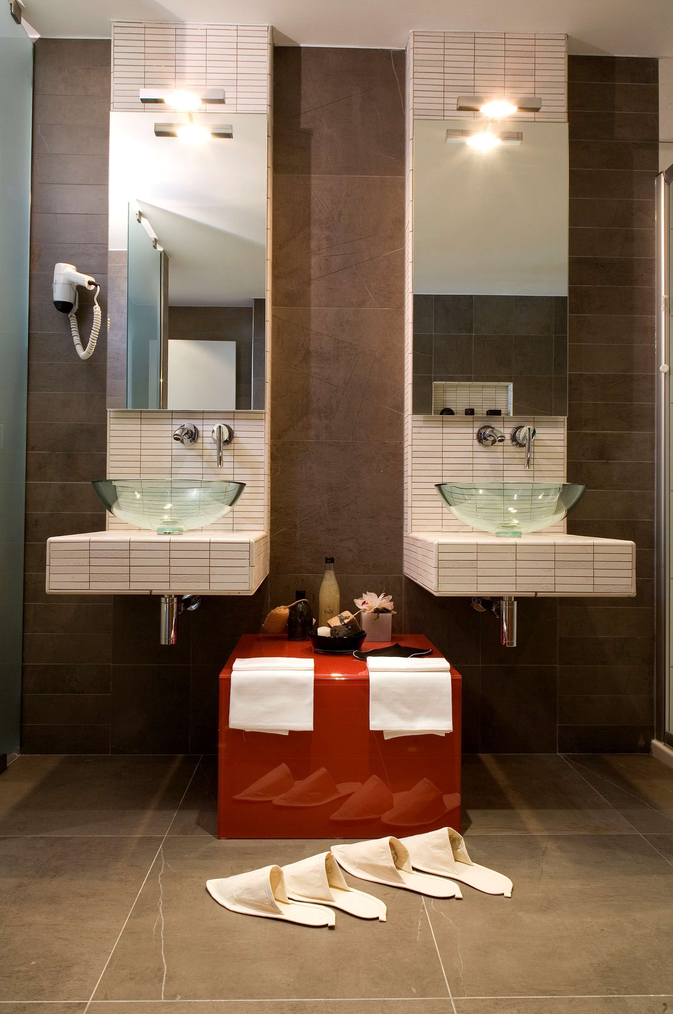 A bathroom with two glass sinks, a red bench, and a towel rack.