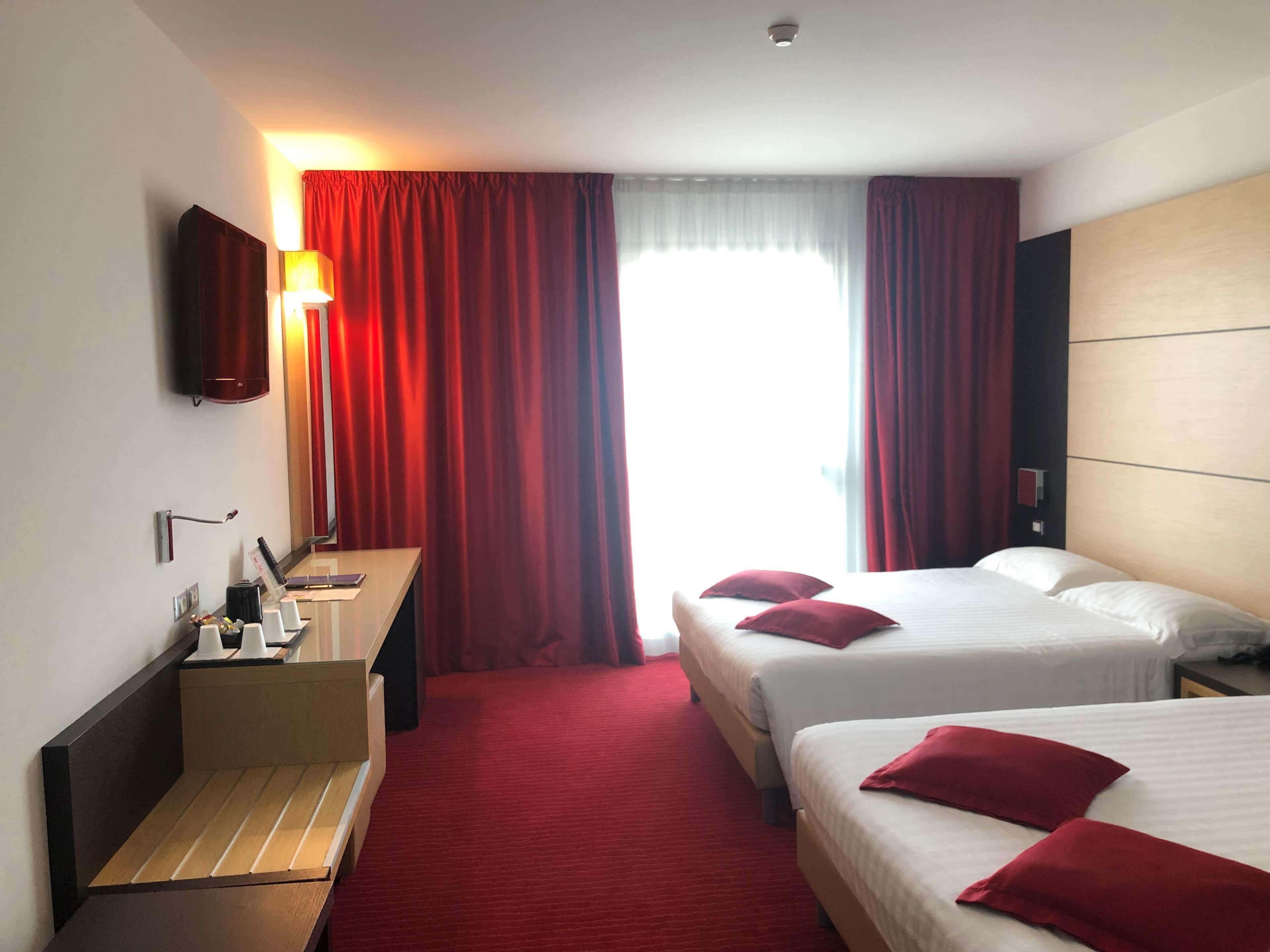 Una camera d'albergo con due letti, una scrivania, uno specchio e una televisione.